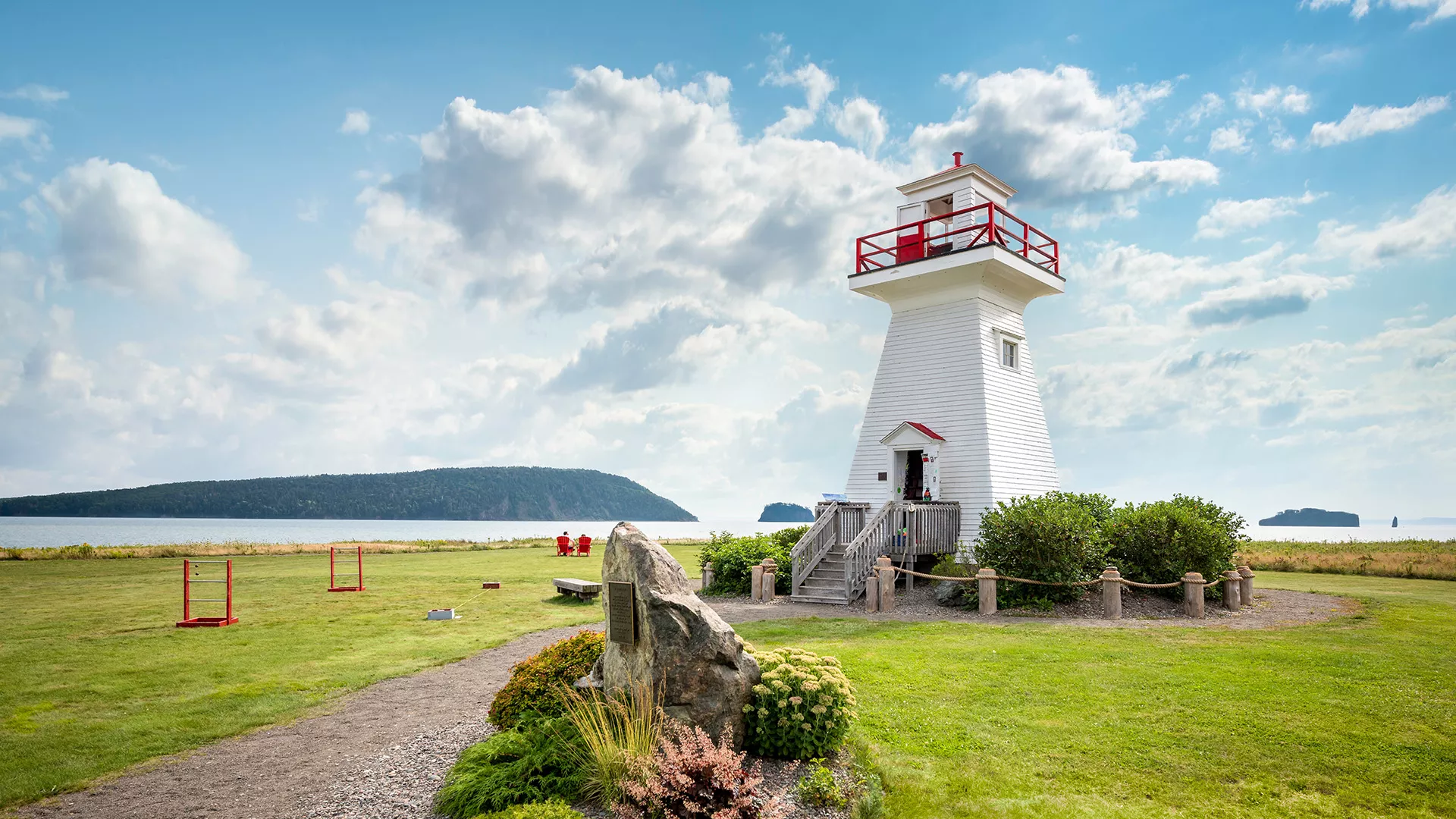 White wooden Sand Point lighthouse with red trim on a grassy headland at Five Islands