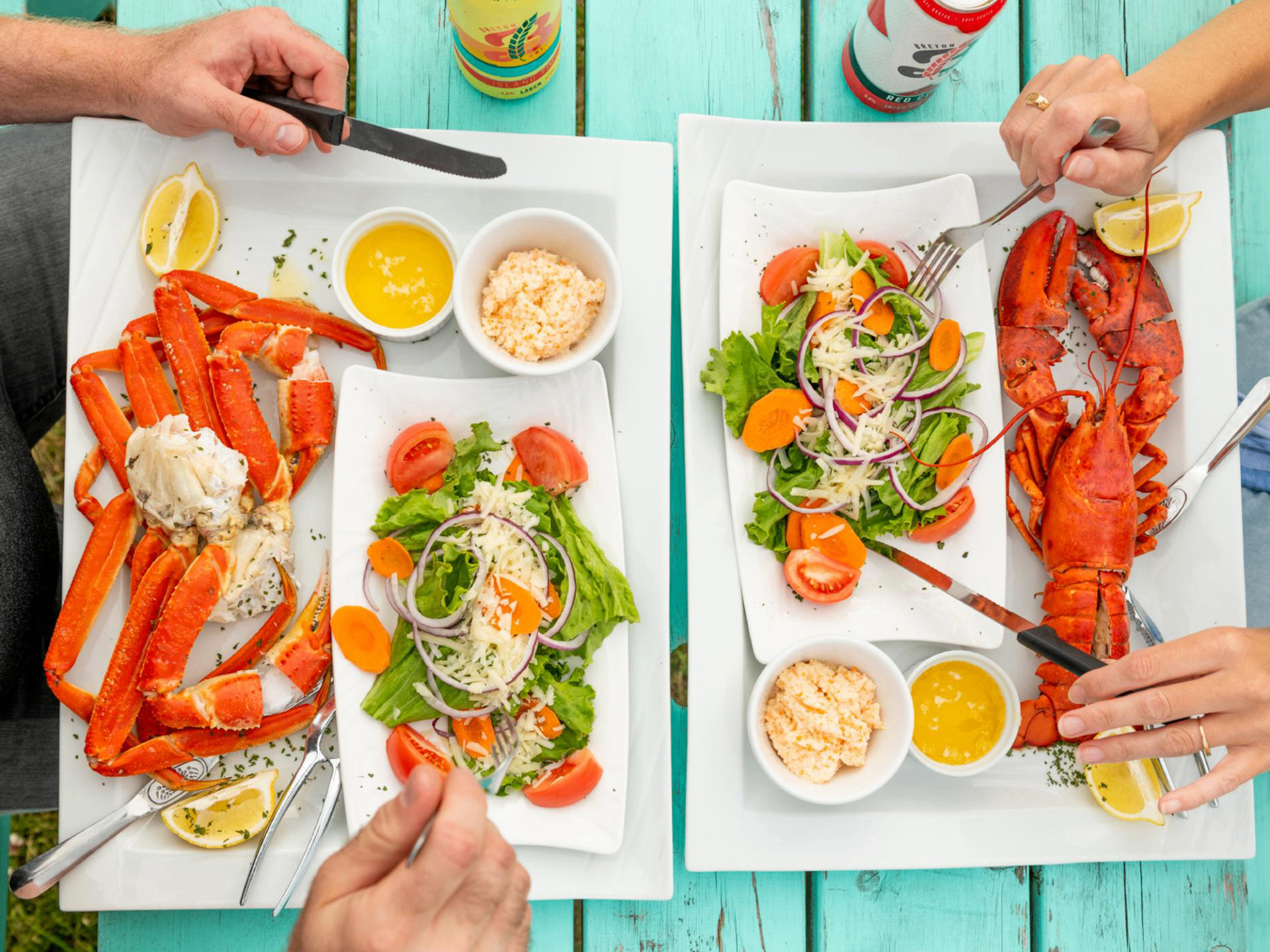 Two seafood platters with lobster, snow crab legs, salad and butter on a turquoise picnic table