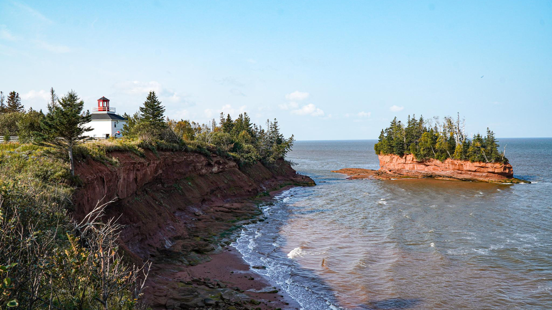 Burntcoat Head Park coastline with red cliffs, a lighthouse, and an island sea stack on the Bay of Fundy