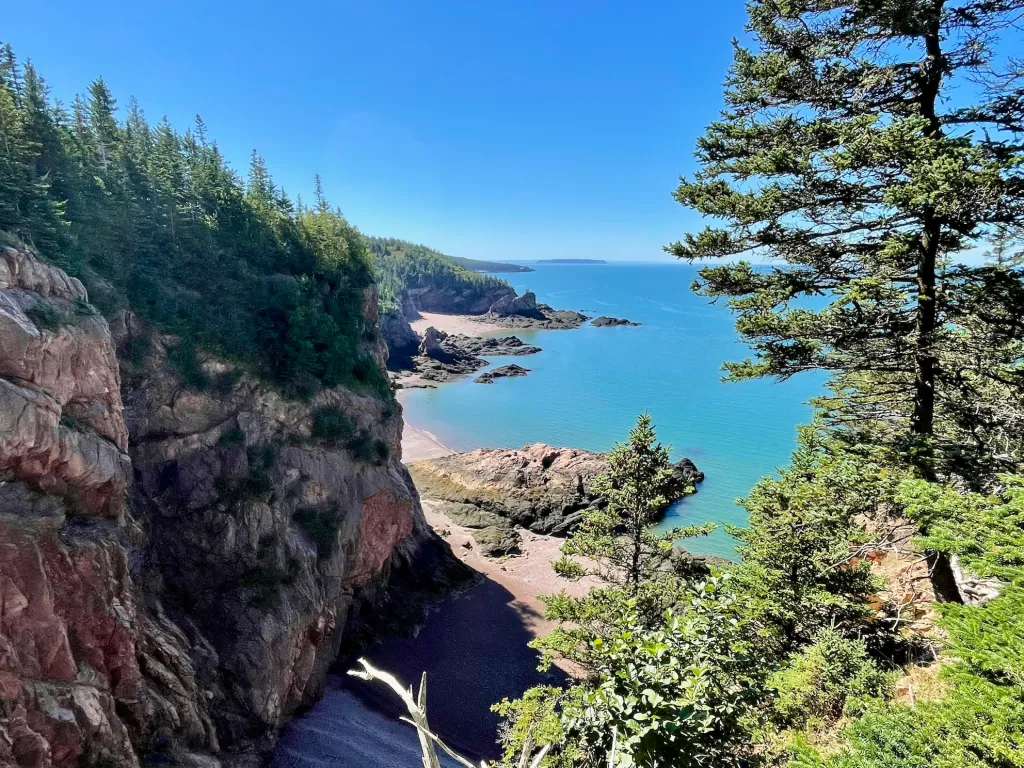 Red sandstone cliffs and evergreens framing a small cove with a sand and pebble beach