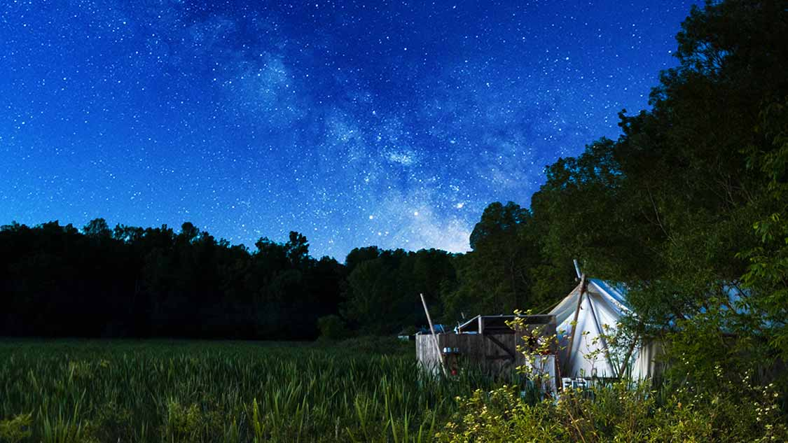 Milky Way over an oTENTik canvas tent glowing in a meadow at Five Islands Provincial Park