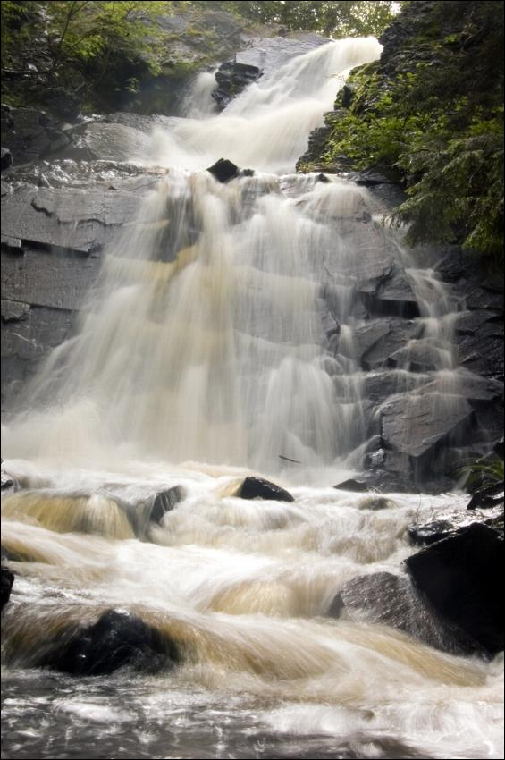 Waterfall tumbling over dark rock into a foaming stream in the Cape Chignecto backcountry