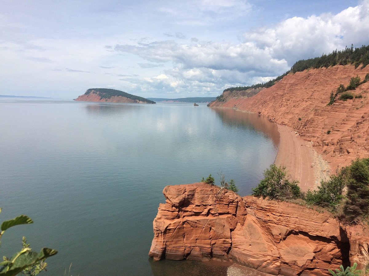 Red sandstone cliffs curving along the shore of the Minas Basin with one of the five islands offshore