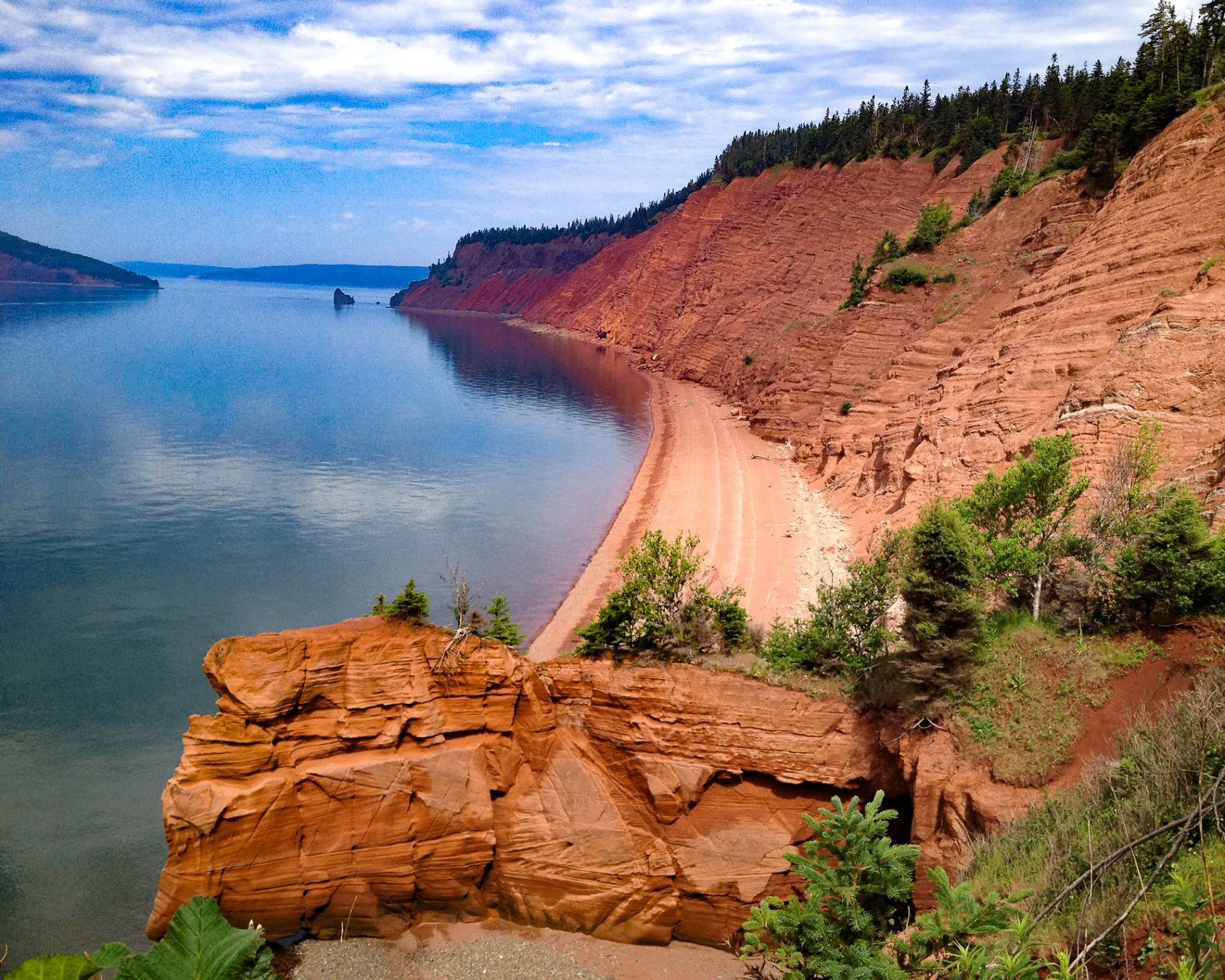 Long red-sand beach beneath layered red sandstone cliffs at Five Islands Provincial Park