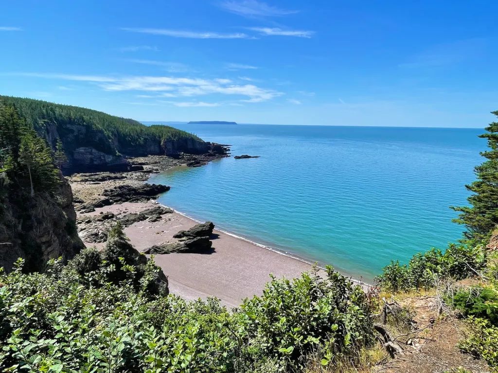 Sweeping view from a cliff-top trail over a cobble beach and turquoise Bay of Fundy water