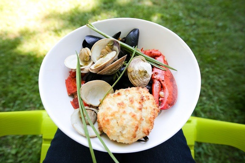 Bowl of lobster, mussels, clams and a biscuit served outdoors on a green chair