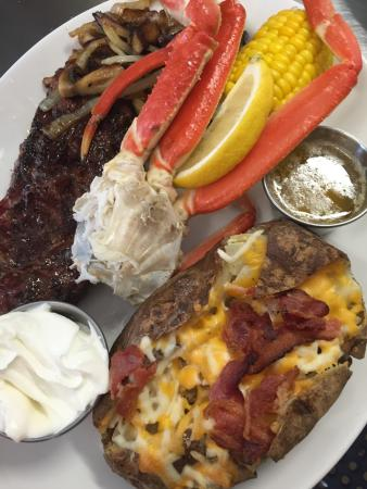 Steak with snow crab legs, corn on the cob, and a loaded baked potato with bacon and cheese