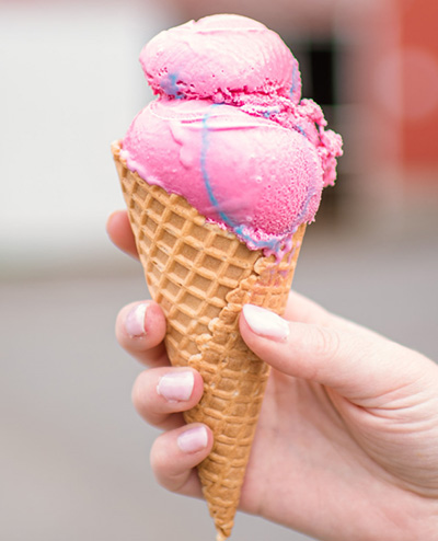 Hand holding a waffle cone with two scoops of bright pink cotton-candy ice cream