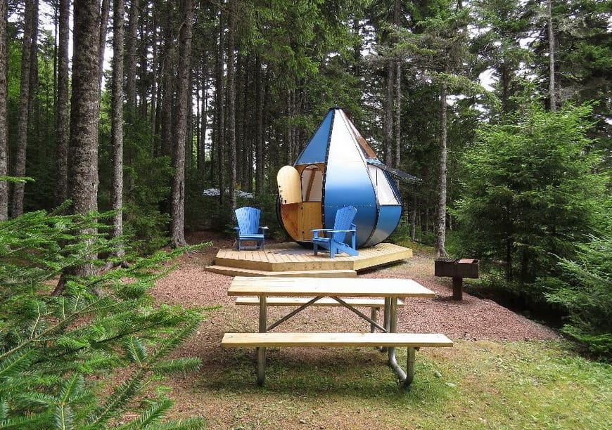 Blue teardrop-shaped oTENTik shelter with Adirondack chairs and a picnic table in the park campground