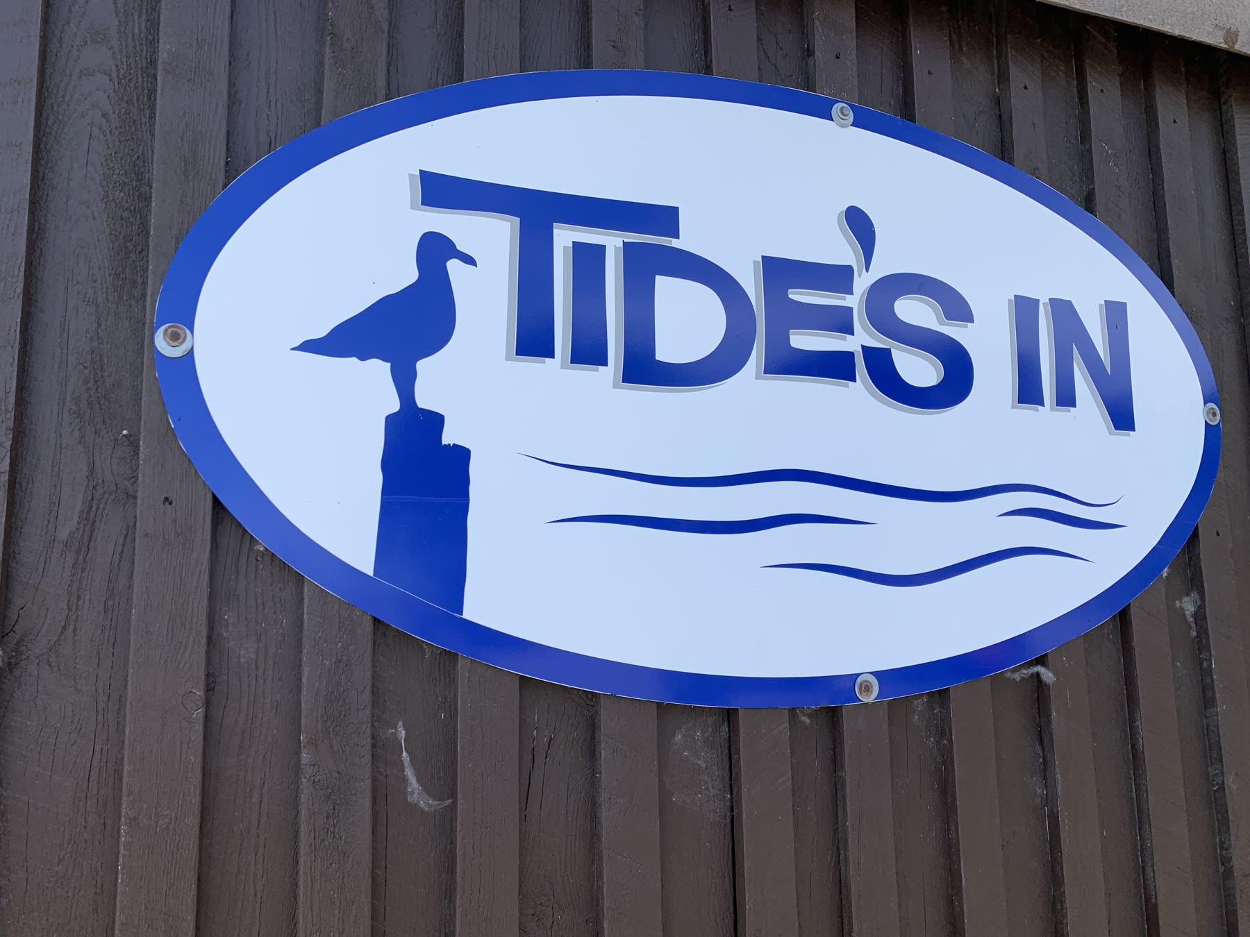 Blue and white Tide's In restaurant sign mounted on brown wood siding